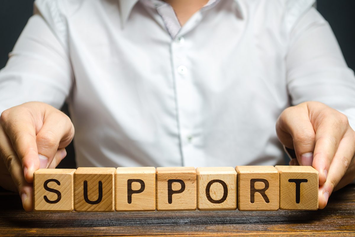 A man's hands arranging wooden blocks to spell out the word SUPPORT
